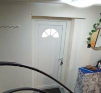 Vstup do rodinného domu s bílými dveřmi, zrcadlem a dekorativními prvky.