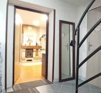 Interiér rodinného domu se schodištěm, podlahou s dřevěným dekorem a krbem.