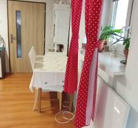 Jídelna v rodinném domě s červeným závěsem, stolem a podlahou s dřevěným dekorem.