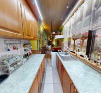 Kuchyně v rodinném domě se skříňkami, spotřebiči a výhledem do zahrady přes velké okno.