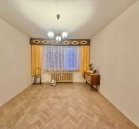 Pokoj v 3pokojovém bytě s podlahou s dřevěným dekorem, záclonami a komodou.