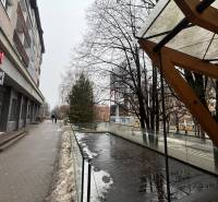 Obchodní prostory v Popradu vedle proskleného zábradlí a mokré dlažby, zasněžený chodník.