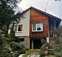 Chata v Modré s dřevěným obkladem a garáží, obklopená zelení.