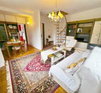 Interiér chaty se spirálovým schodištěm, televizí a stolem na podlaze s dřevěným dekorem.