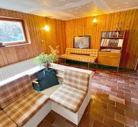 Interiér chaty s obývacím pokojem, rustikálním nábytkem a cihlovou podlahou.