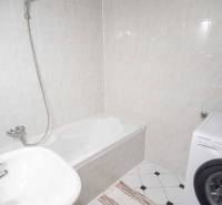 Koupelna se sprchovou vanou, umyvadlem a pračkou ve 4pokojovém bytě.