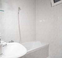 Koupelna s vanou a pračkou ve 4-pokojovém bytě. Stěny pokryté světlými obklady.