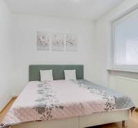 Ložnice se světlou postelí, podlahou s dřevěným dekorem a ozdobnými obrazy ve 4pokojovém bytě.