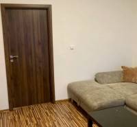 Obývací pokoj s pohovkou, dřevěná dekor podlaha a tmavé dveře ve 3-pokojovém bytě.