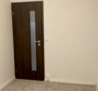 Pokoj v 3-pokojovém bytě s kobercovou podlahou a tmavými dveřmi.