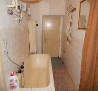 Koupelna v rodinném domě se starší vanou a obkladem na stěnách.