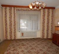 Pokoj v rodinném domě s květinovými vzorovanými tapetami a centrálním lustrem.