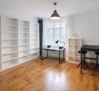 Prostorný pokoj s regály, stolem a podlahou s dřevěným dekorem v 2-pokojovém bytě.