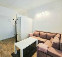 Garsonka s rohovou sedačkou, bílým stolkem a podlahou s dřevěným dekorem.