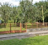 Dům a brána obklopené stromy na pozemcích pro bydlení v Lastomíru.