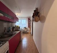 Kuchyně v 2-pokojovém bytě s podlahou s dřevěným dekorem, s jídelním koutem v pozadí.