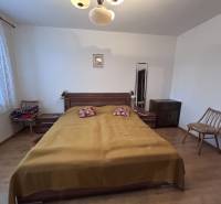 Ložnice v 2pokojovém bytě s postelí, židlemi a podlahou s dřevěným dekorem.