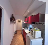 Kuchyně s červenými skříňkami a podlahou s dřevěným dekorem v 2pokojovém bytě.