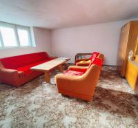 Obývací pokoj v rodinném domě s oranžovou pohovkou, dřevěným stolkem a vitrínou.