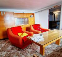 Obývací pokoj v rodinném domě se staršími křesly, stolem a prosklenou skříní.