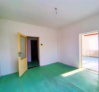 Interiér rodinného domu s otevřenými dveřmi, bílými stěnami a zelenou podlahou.