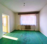 Pokoj v rodinném domě s radiátorem, zelená podlaha, výhled na střechy.