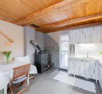 Kuchyně v chatě s dřevěným stropem, pecí a bílým nábytkem.