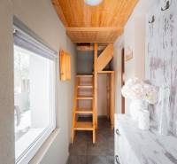 Interiér chaty s dřevěným schodištěm a oknem s výhledem na exteriér.