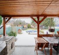 Dřevěný přístřešek u chaty v Handlové, s výhledem na zasněženou zahradu a ploty.