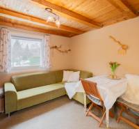 Interiér chaty s rohovou sedačkou, stolem a dřevěným stropem.