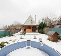 Zasněžená zahrada s chatou v Handlové a prázdným bazénem v popředí.