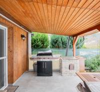 Dřevěné obložení a gril na terase chaty v Handlové, vedle zelených keřů.