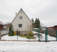 Chata v Handlové s trochou sněhu na dvoře, obklopená zelení a plotem.