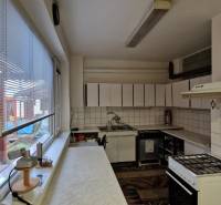 Kuchyně v rodinném domě se spotřebiči, dlaždicemi a oknem s výhledem na terasu.