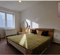 Ložnice s manželskou postelí, zelenou přikrývkou, nočním stolkem a zrcadlem v rodinném domě.