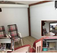 Letní terasa rodinného domu s posezením a podlahou s dřevěným dekorem.