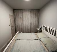 Světlá ložnice v 2pokojovém bytě s prostornou postelí a skříní s dřevěným dekorem.