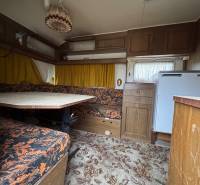 Interiér obytného prostoru s kobercovou podlahou, sedací soupravou a stolem.