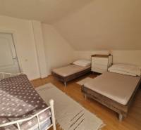 Ložnice v rodinném domě se třemi postelemi a podlahou s dřevěným dekorem.