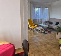 Obývací pokoj v rodinném domě s oknem, žlutým křeslem a stolkem.