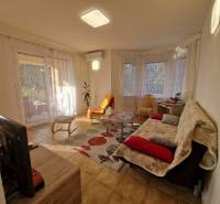 Obývací pokoj rodinného domu s televizorem, pohovkou, stolkem a velkými okny se závěsy.