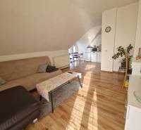 Podkrovní obývací pokoj v rodinném domě s pohovkou, jídelním stolem a podlahou s dřevěným dekorem.