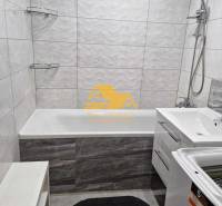 Koupelna v 3-pokojovém bytě s vanou, sprchou a pračkou na bílých obkladech.