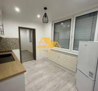 Kuchyně v 1-pokojovém bytě s podlahou s dřevěným dekorem a bílými elektrospotřebiči.