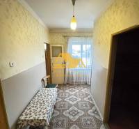 Chodba v rodinném domě s kobercovým dekorem a stolem, okno na konci místnosti.