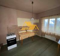 Kuchyně v rodinném domě se sporákem, stolem, záclonou a světlým dekorem stěn.