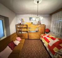 Obývací pokoj v rodinném domě s kobercem, pohovkou a skříní s porcelánem.