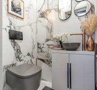 Koupelna v 2-pokojovém bytě s mramorovými stěnami, stylovým umyvadlem a dekoracemi.