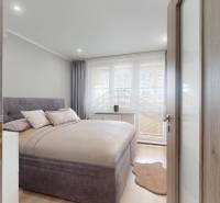 Ložnice v 3-pokojovém bytě s postelí, závěsy a podlahou s dřevěným dekorem.