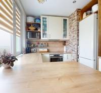 Kuchyně ve 3-pokojovém bytě se světlou kuchyňskou linkou a podlahou s dřevěným dekorem.